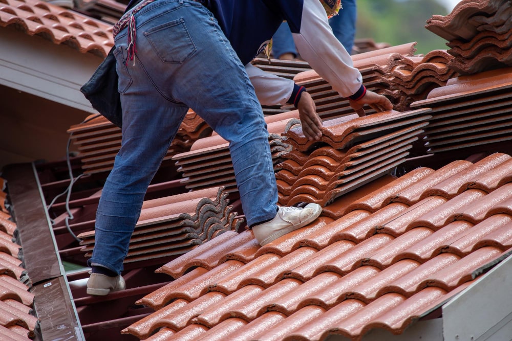 A close-up of a roofing professional installing interlocking red terracotta tiles on a sloped residential roof.